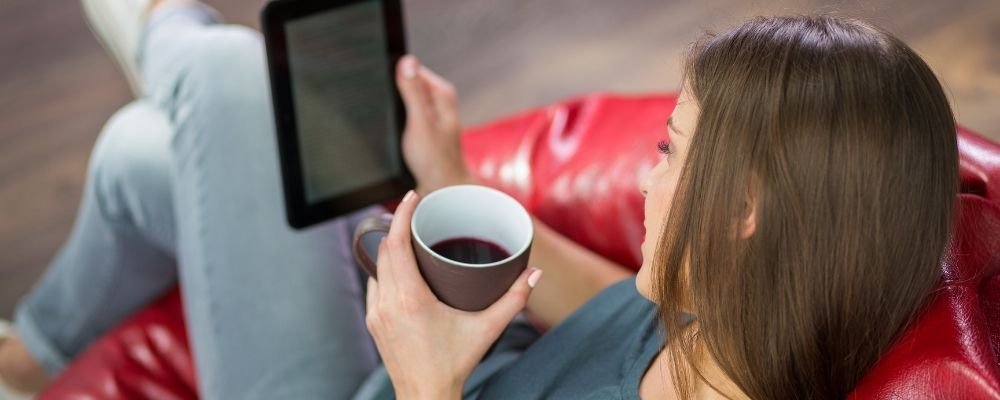 Vrouw zit op een stoel met koffie en leest een ebook