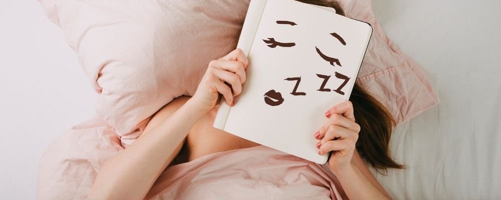 Vrouw ligt in bed met een bordje met een slapend gezicht erop voor haar gezicht