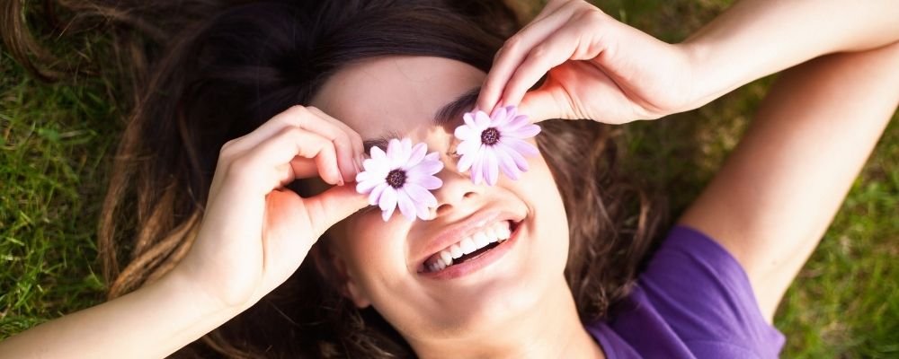 Vrouw houdt bloemetjes voor haar ogen en lacht erg breed